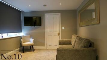 A room with a beige carpet, a white door, a television mounted on the wall, and a large mirror.