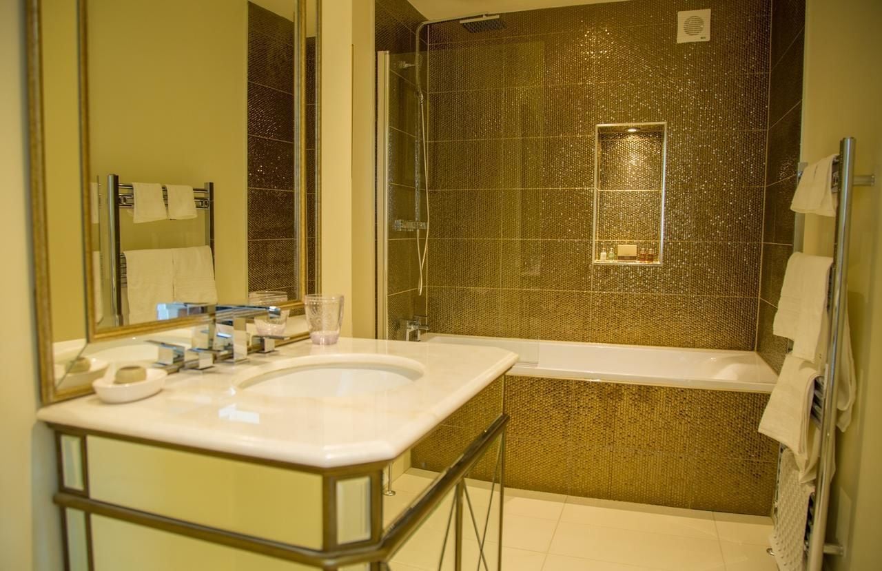 Un baño con un espejo grande, un lavamanos, una bañera y una ducha con pared texturizada.