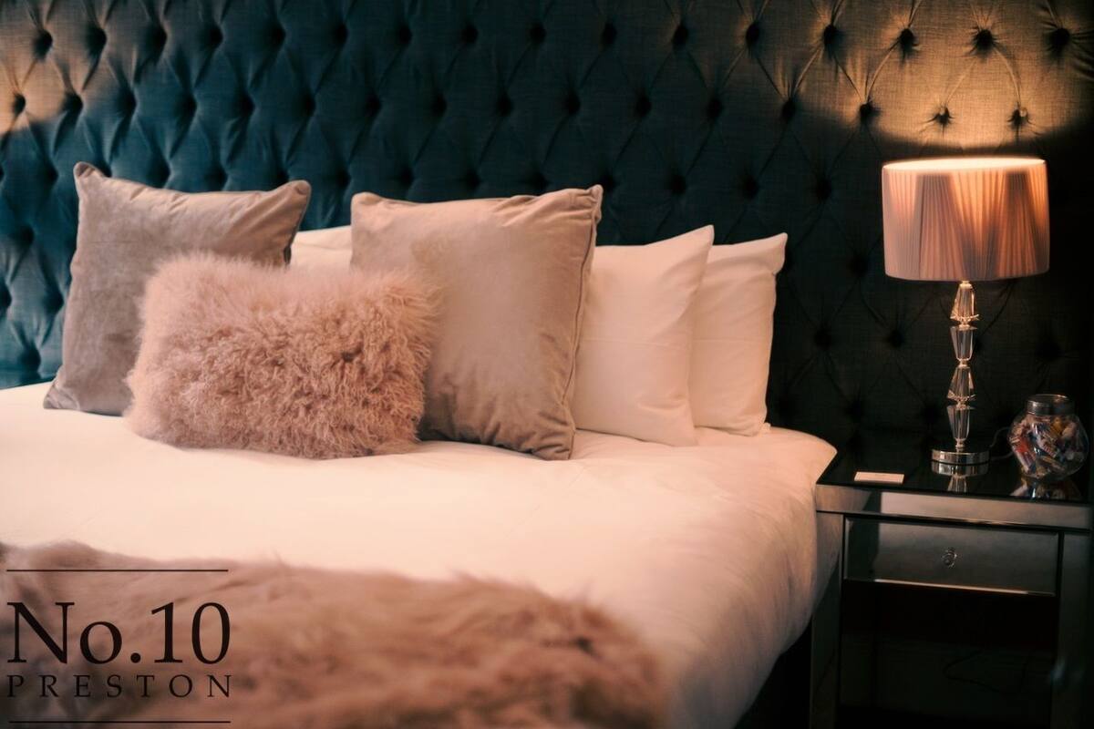 A bedroom with a tufted headboard, a bed with white linens, and a nightstand with a lamp and decorative items.
