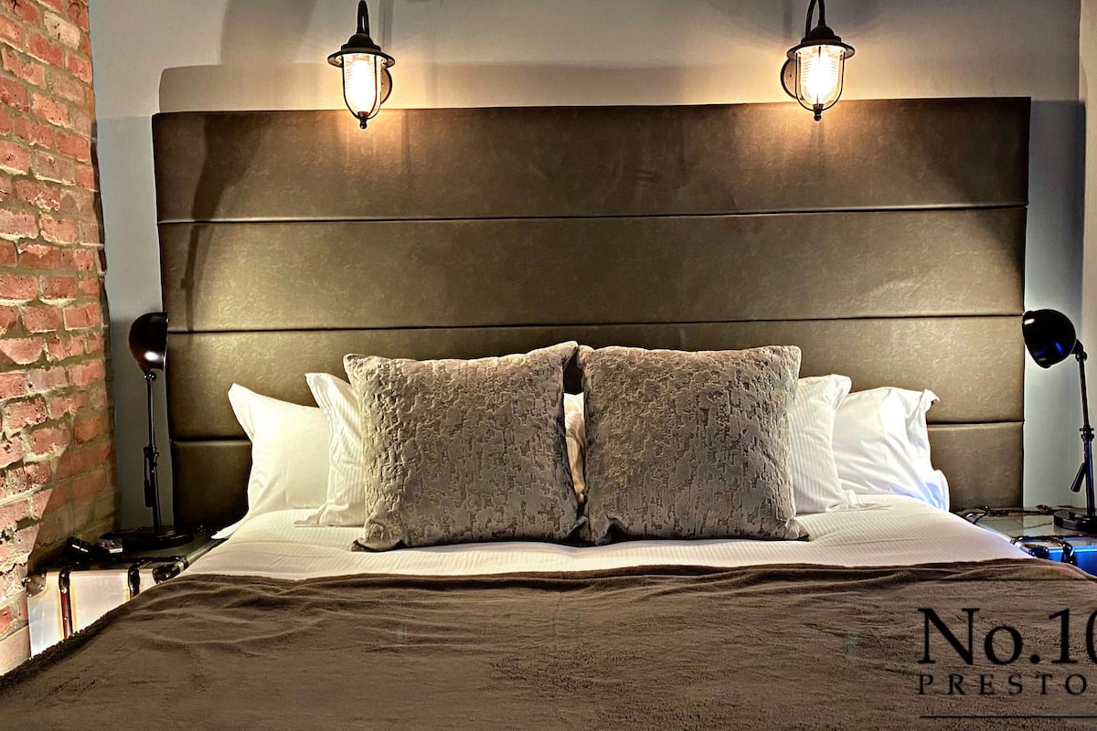 A hotel room with a large bed, two bedside lamps, a brick wall, and a window with blue lighting.