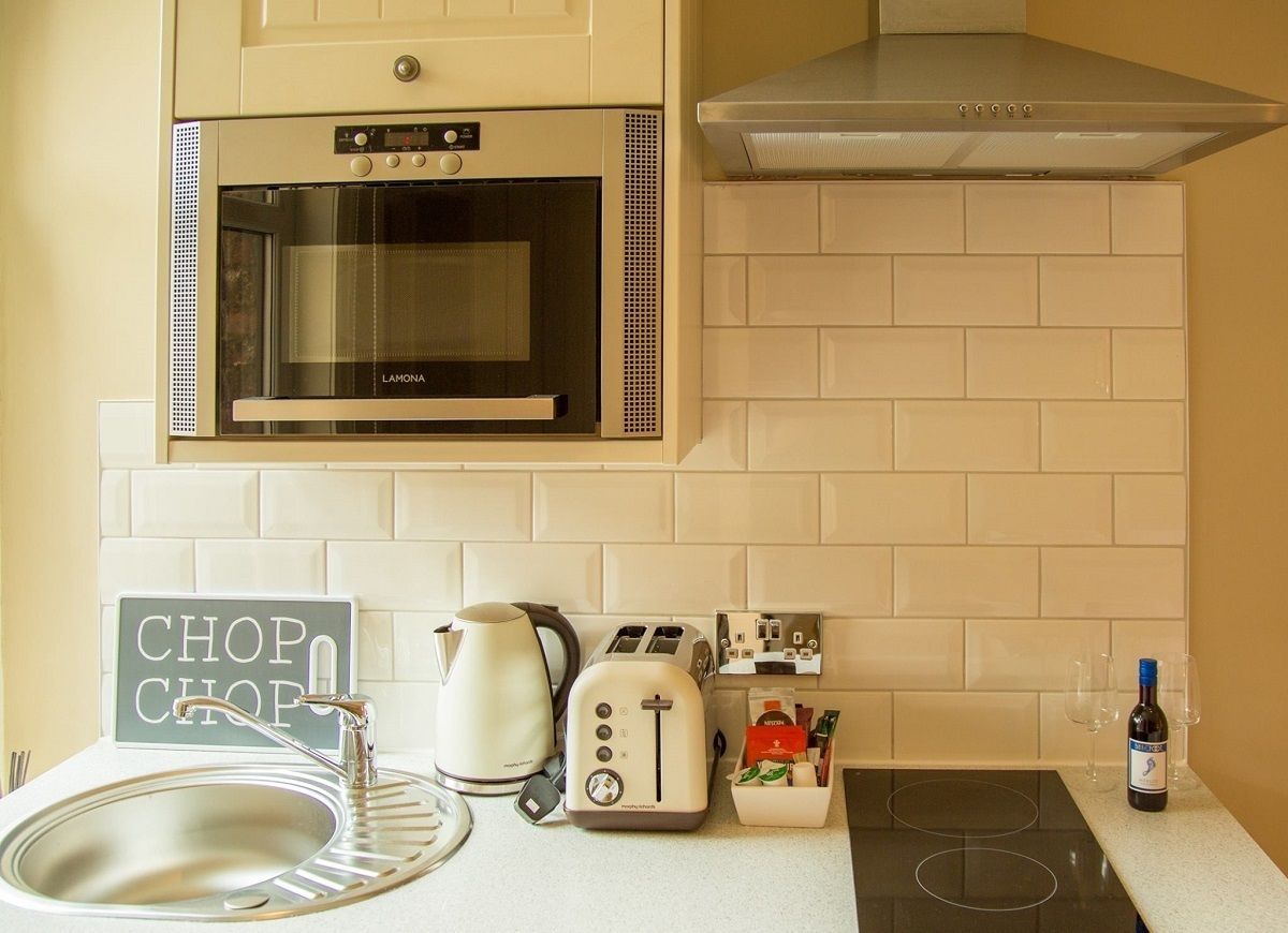 A kitchen with a built-in oven, a toaster, a kettle, a sink, and a wine bottle.