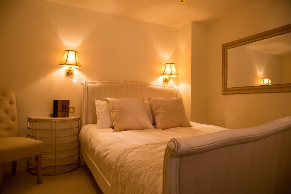 A hotel room with a bed, two wall-mounted lamps, a round side table, a chair, and a mirror.
