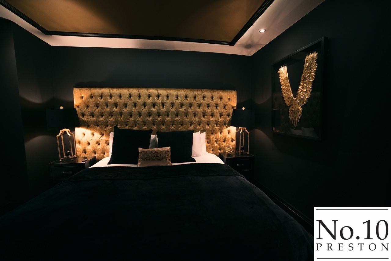 Quarto moderno com cabeceira estofada, uma cama grande, duas mesas de cabeceira com abajures e uma obra de arte emoldurada na parede.
