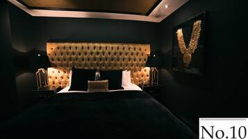 Quarto moderno com cabeceira estofada, uma cama grande, duas mesas de cabeceira com abajures e uma obra de arte emoldurada na parede.