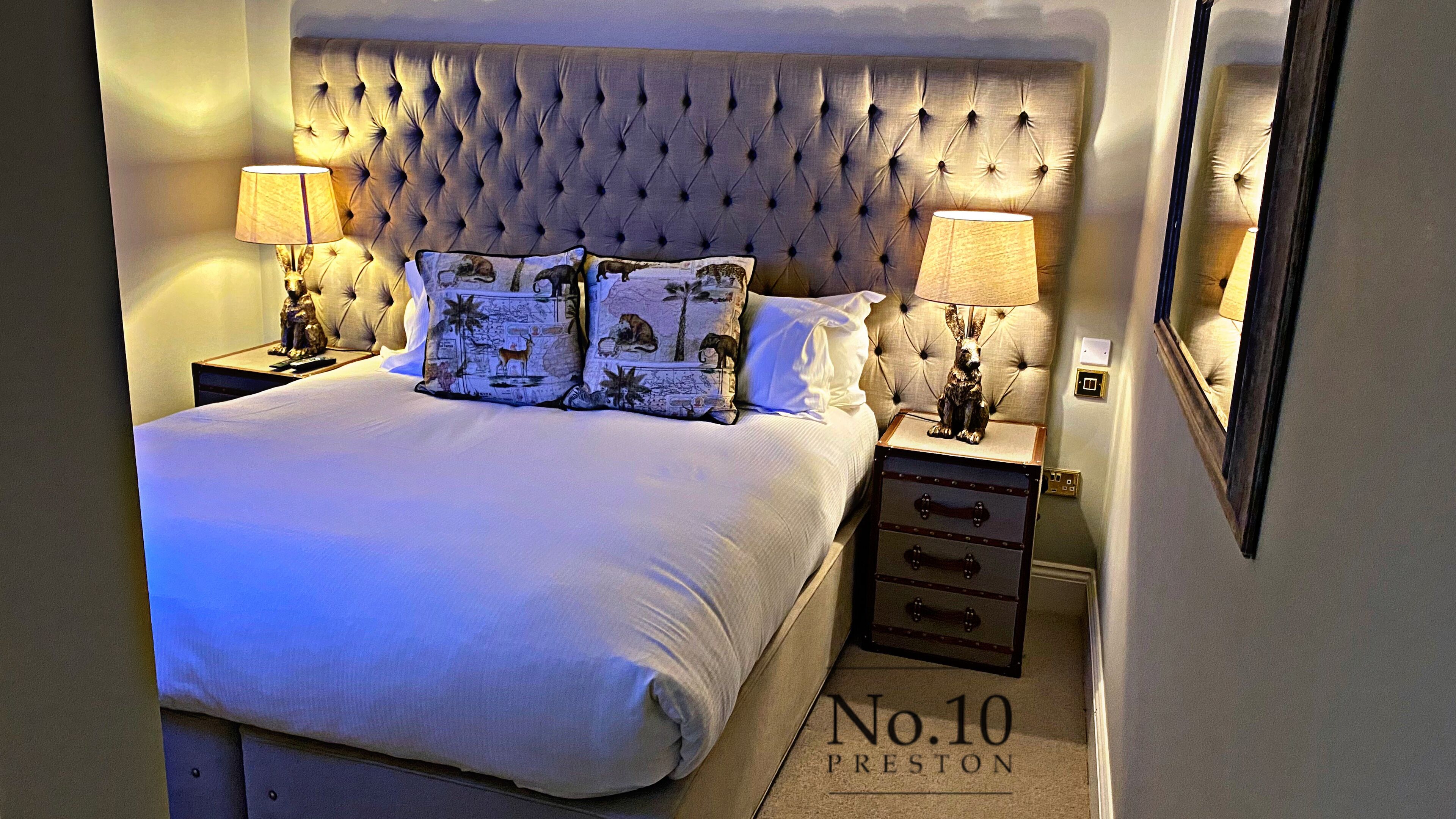 A neatly made bed with a tufted headboard, two bedside lamps, and a decorative pillow with animal prints.