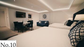 A modern hotel room with a large bed, a desk, a sofa, and a TV mounted on the wall.