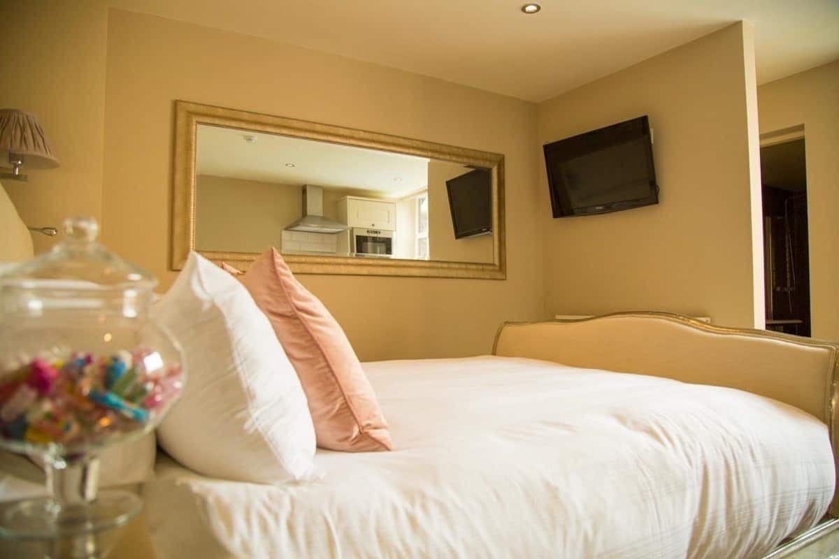 A hotel room with a bed, a large mirror, a television, and a glass jar with colorful items.