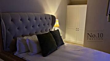 A bedroom with a tufted headboard, a bedside lamp, a wardrobe, and a sign reading "No.10 Preston".