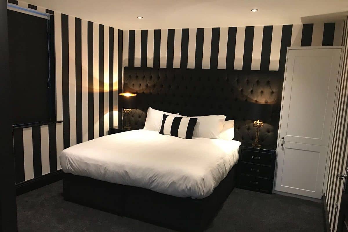 A bedroom with a large bed, black and white striped walls, and a tufted headboard.