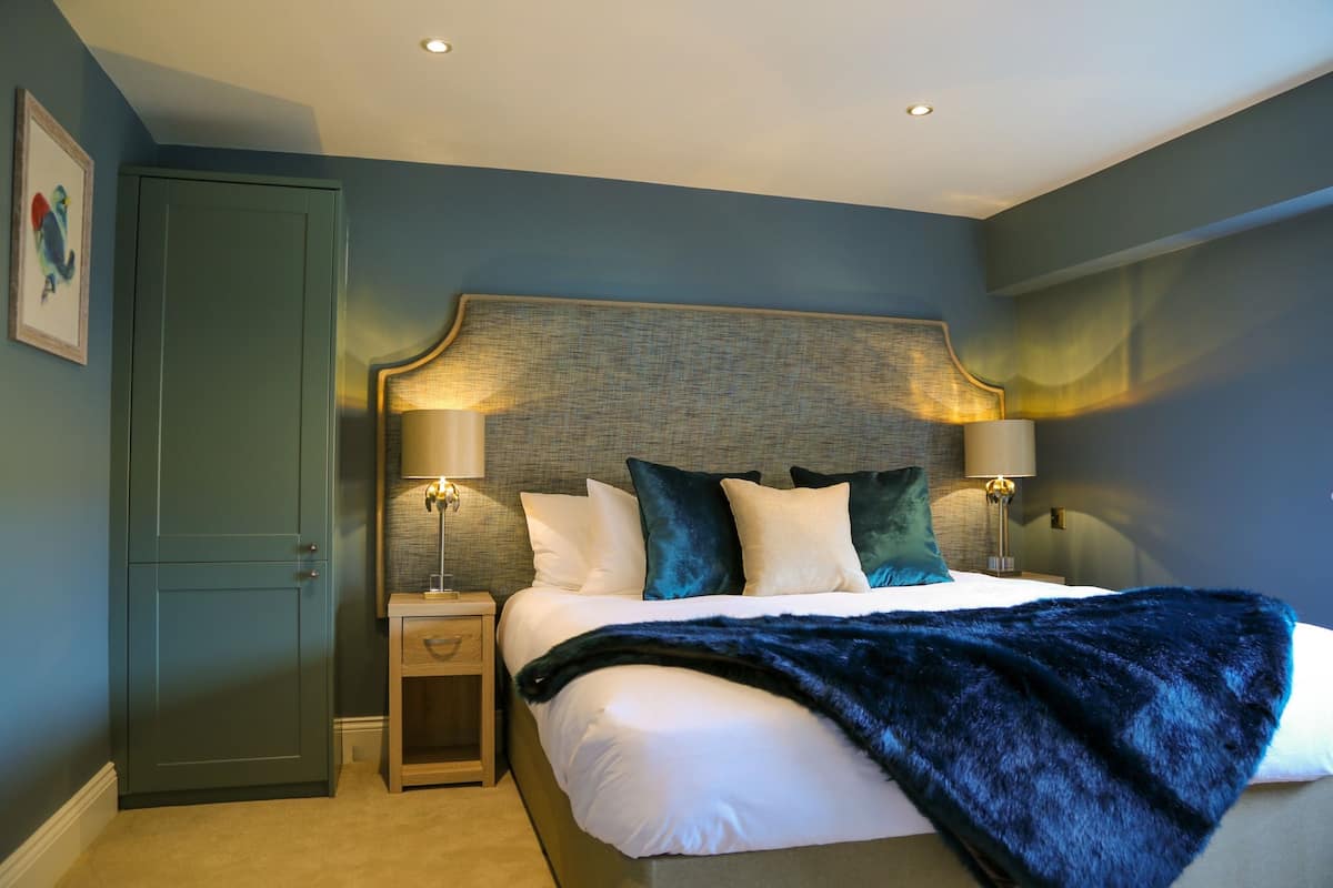A bedroom with a bed, two bedside lamps, a nightstand, a wardrobe, and a framed picture on the wall.