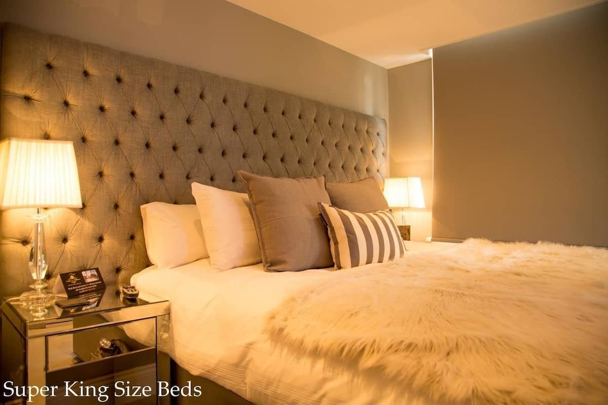 A king-sized bed with a tufted headboard, two bedside lamps, and a fluffy white throw blanket.