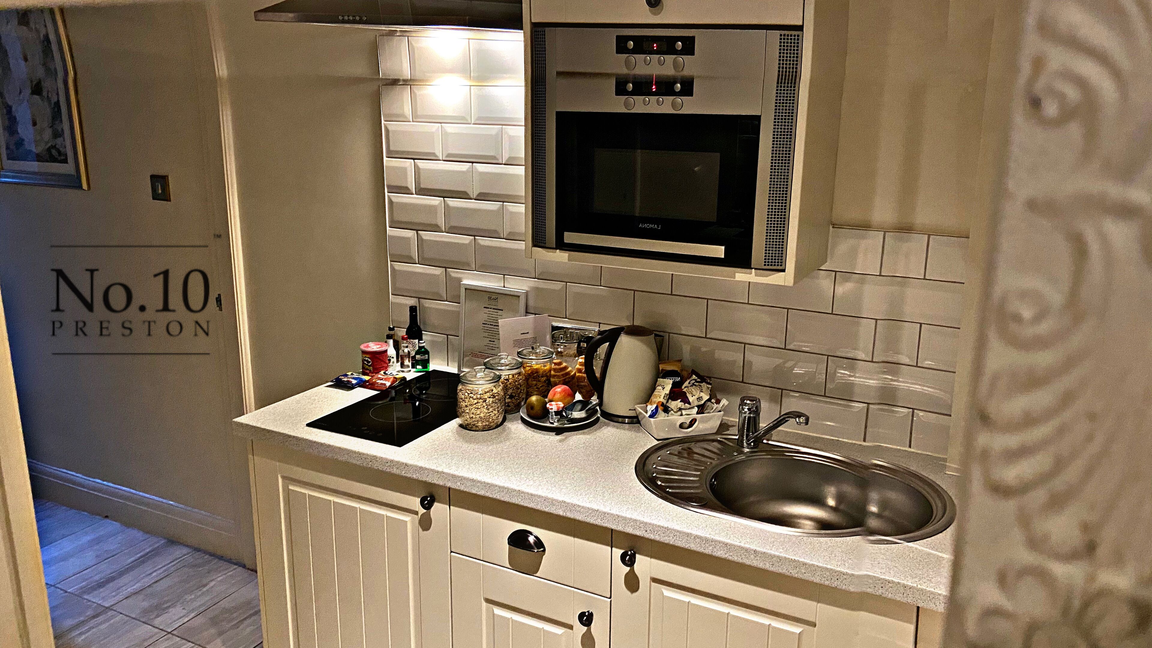 Cocina compacta con microondas, horno y lavaplatos. Hay varios alimentos y condimentos en la encimera.