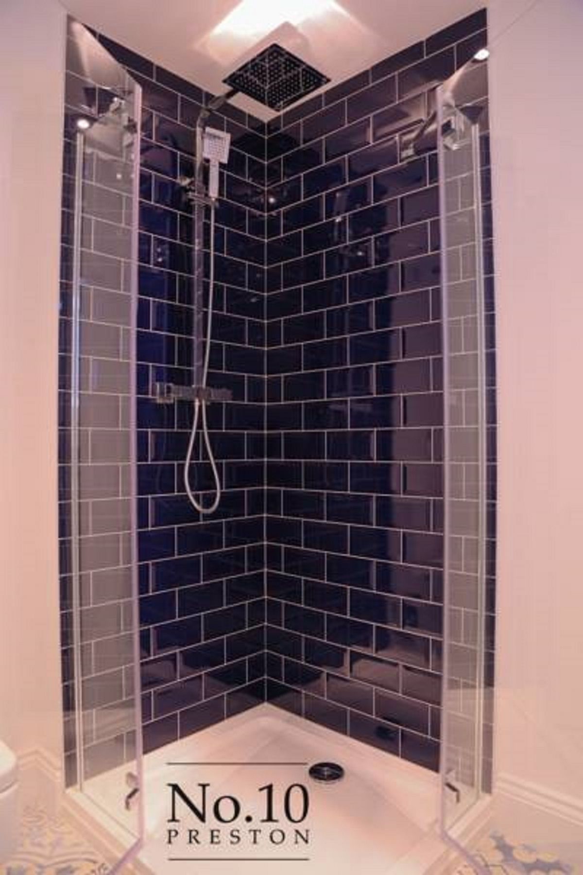 Ducha en esquina con azulejos oscuros y mampara de cristal.