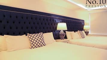 Camera d'albergo con una testiera imbottita blu scuro, due letti con biancheria bianca e un comodino con una lampada.