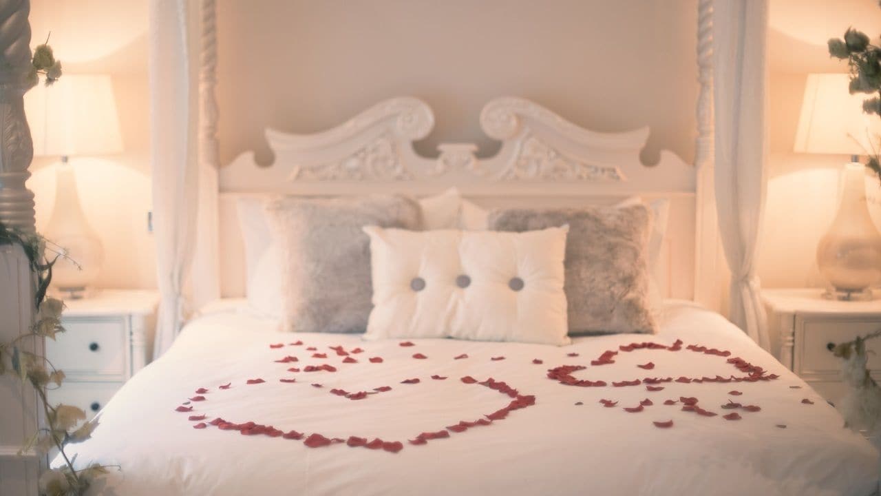 A bed with a heart-shaped arrangement of rose petals and a white bedspread.