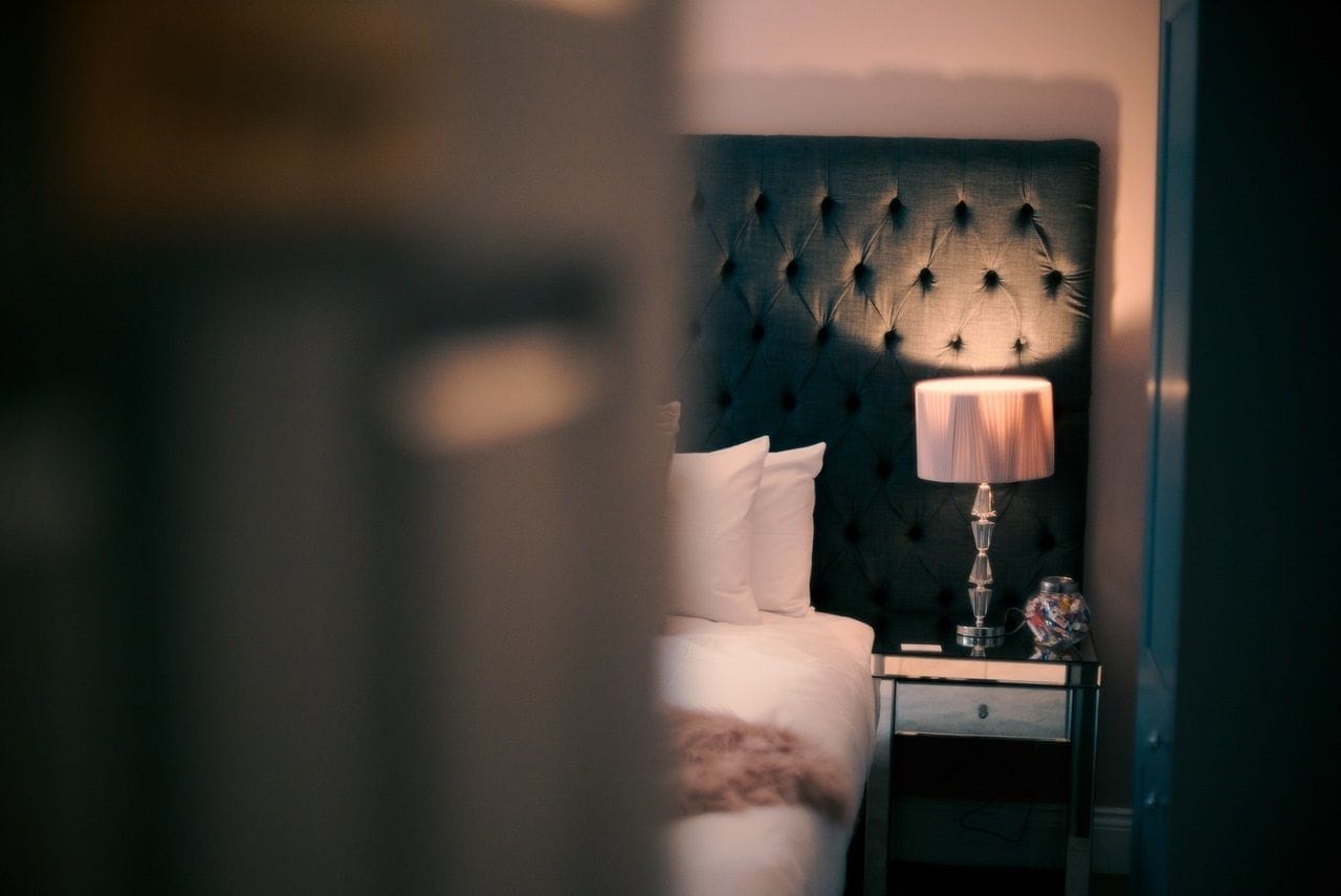 A bedroom with a tufted headboard, a bedside lamp, and a nightstand with a decorative item.