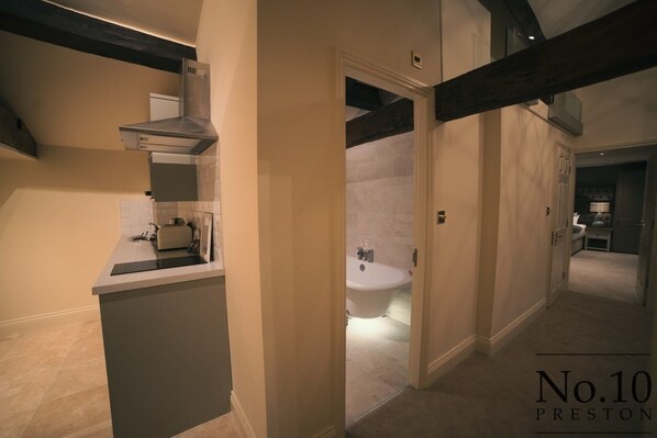 Una cocina moderna con estufa integrada, una pequeña isla y vista a un baño con bañera blanca.
