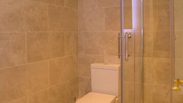 Un baño con azulejos color beige, un inodoro y una zona de ducha con mampara de vidrio.