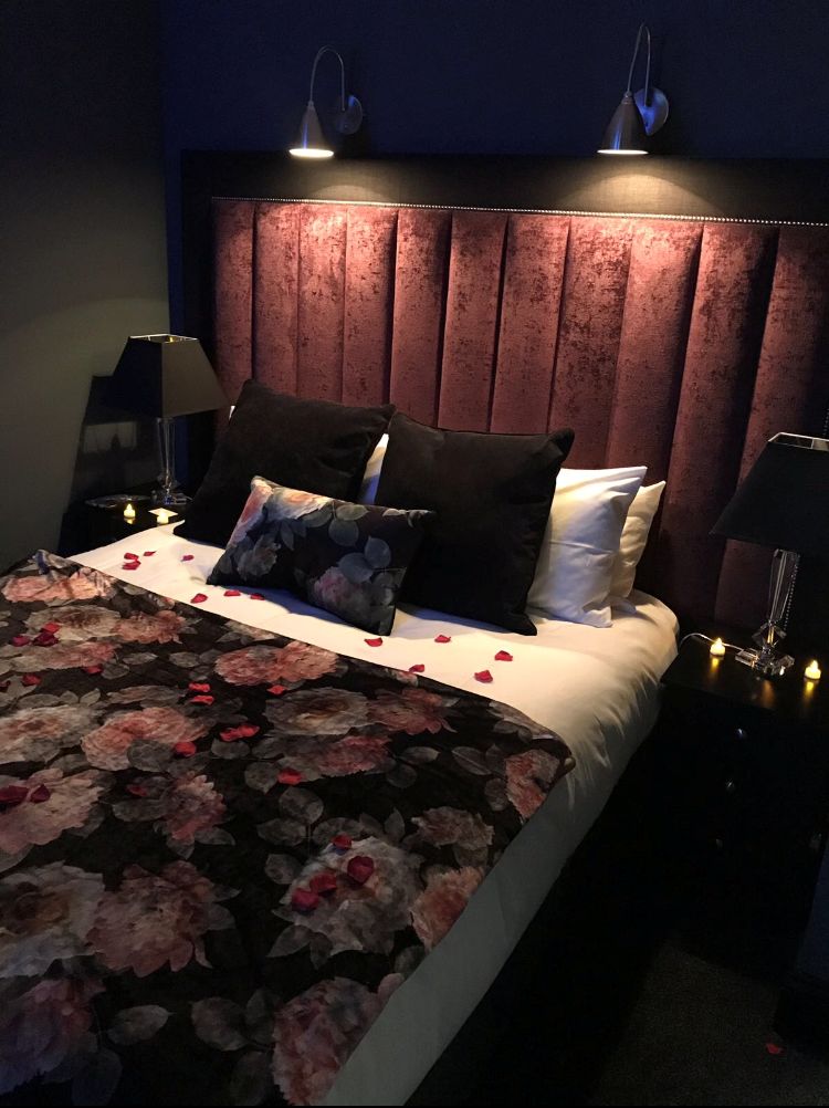 Un letto con una coperta a fiori, due lampade sui comodini e una testiera con pannelli verticali.