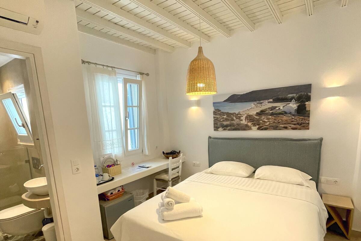 Quarto com uma cama, uma escrivaninha, um espelho e um quadro de uma praia.