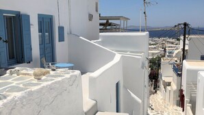 A narrow, white-walled street with blue doors and a stone-paved path leading to a view of the sea. - Hotel Lefteris (Mykonos)