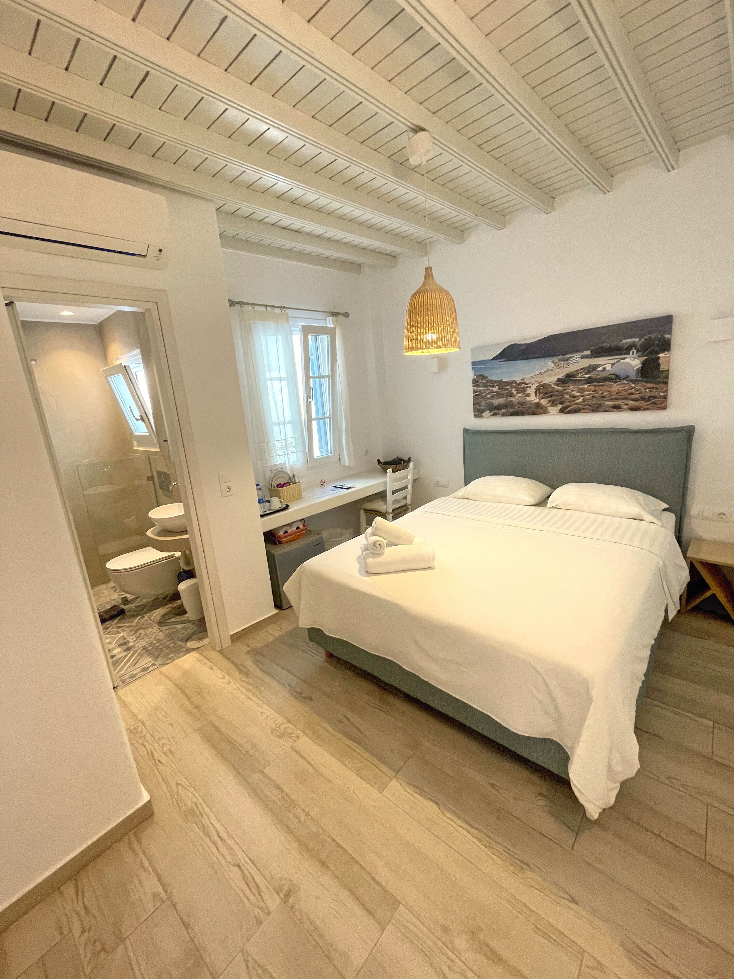 A bedroom with a bed, a desk, and a bathroom.