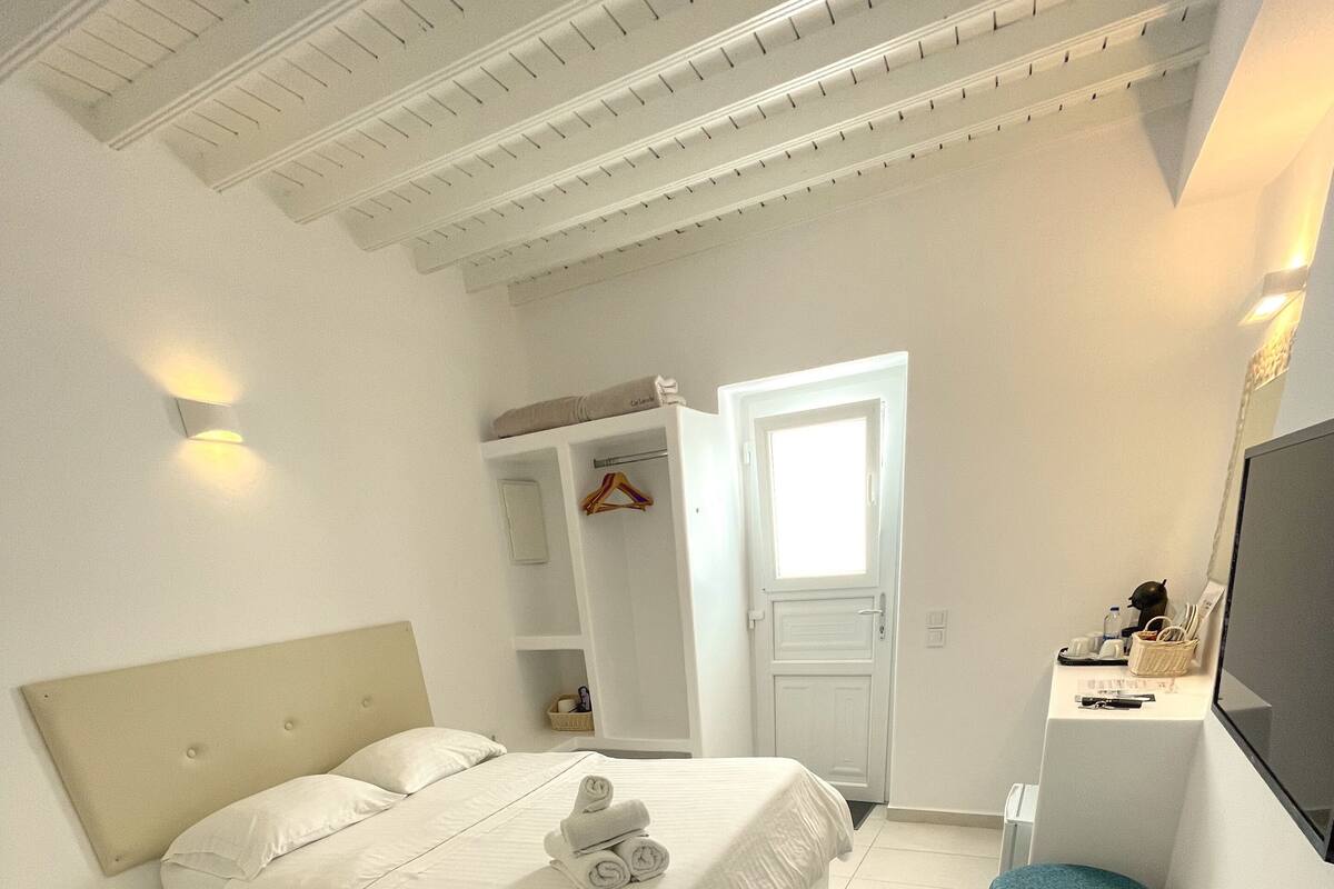 Quarto de hotel com uma cama, uma mesa, uma cadeira, um guarda-roupa e área de chuveiro.