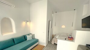 A compact hotel room with a teal sofa, a small wooden table, a white desk, and a patterned floor. - Hotel Lefteris (Mykonos)