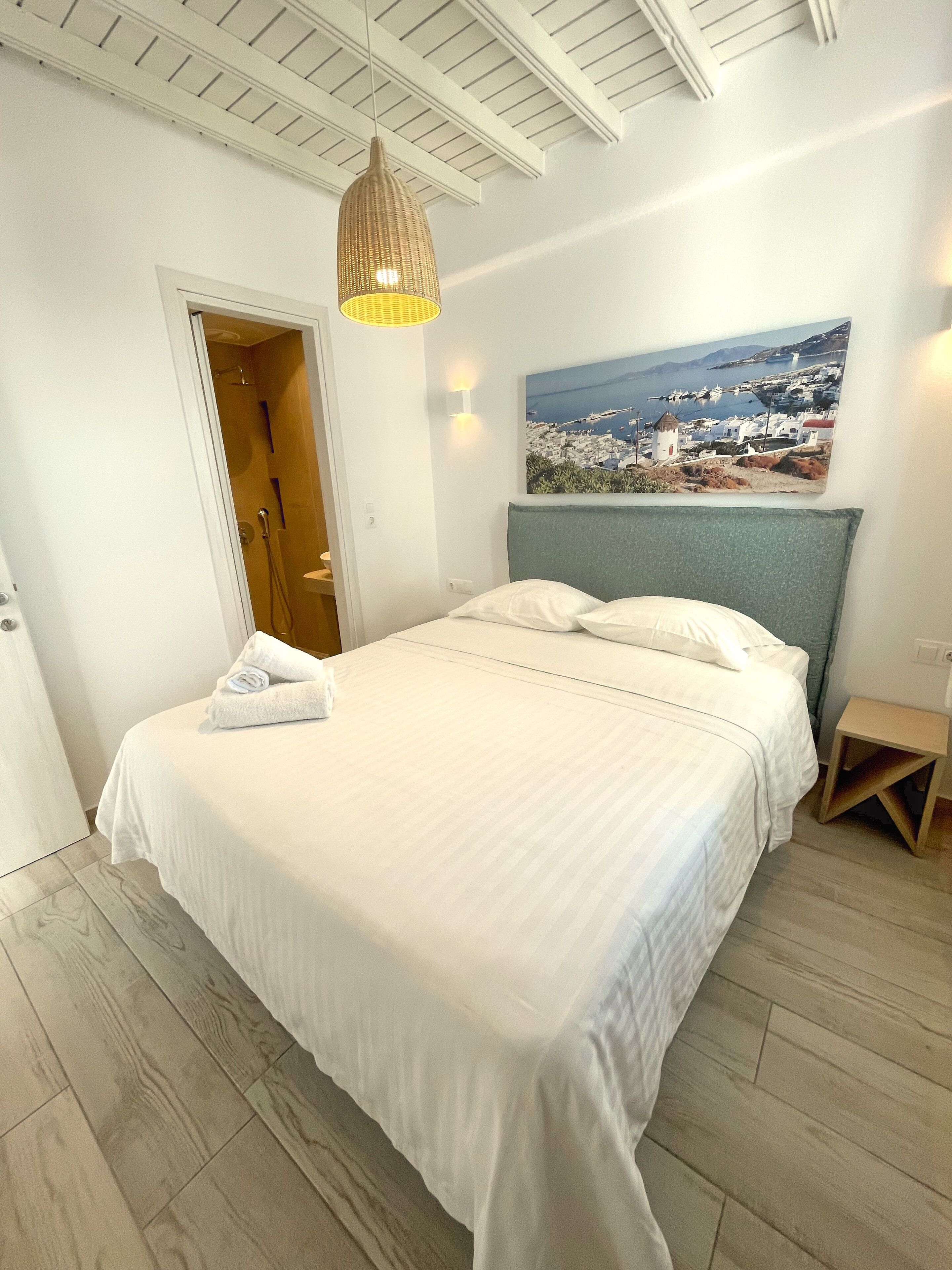 Un dormitorio con cama, suelo de madera, puerta, lámpara colgante y un cuadro en la pared.
