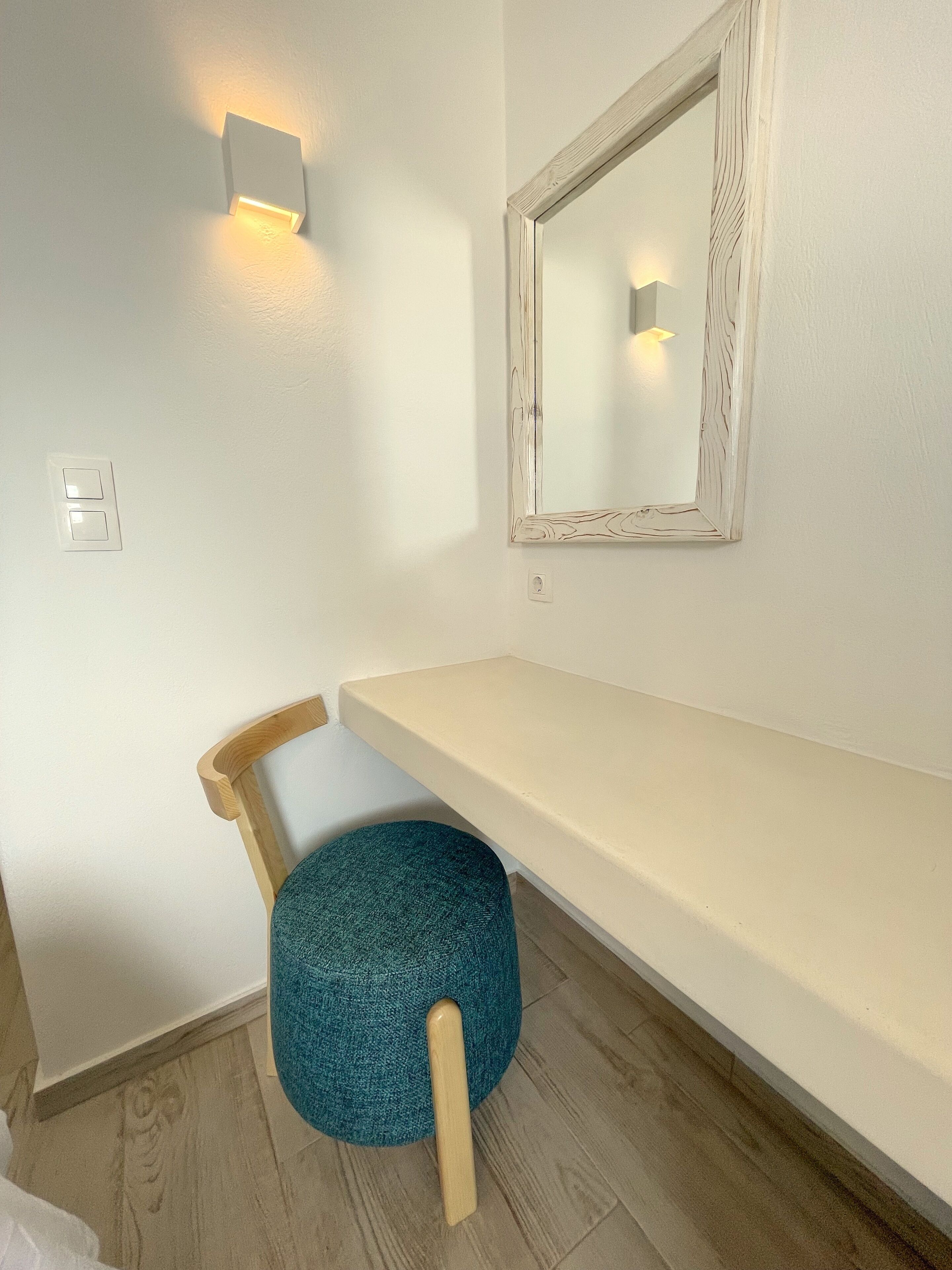 A room with a wooden chair, a white bench, a mirror with a wooden frame, and a wall-mounted light.