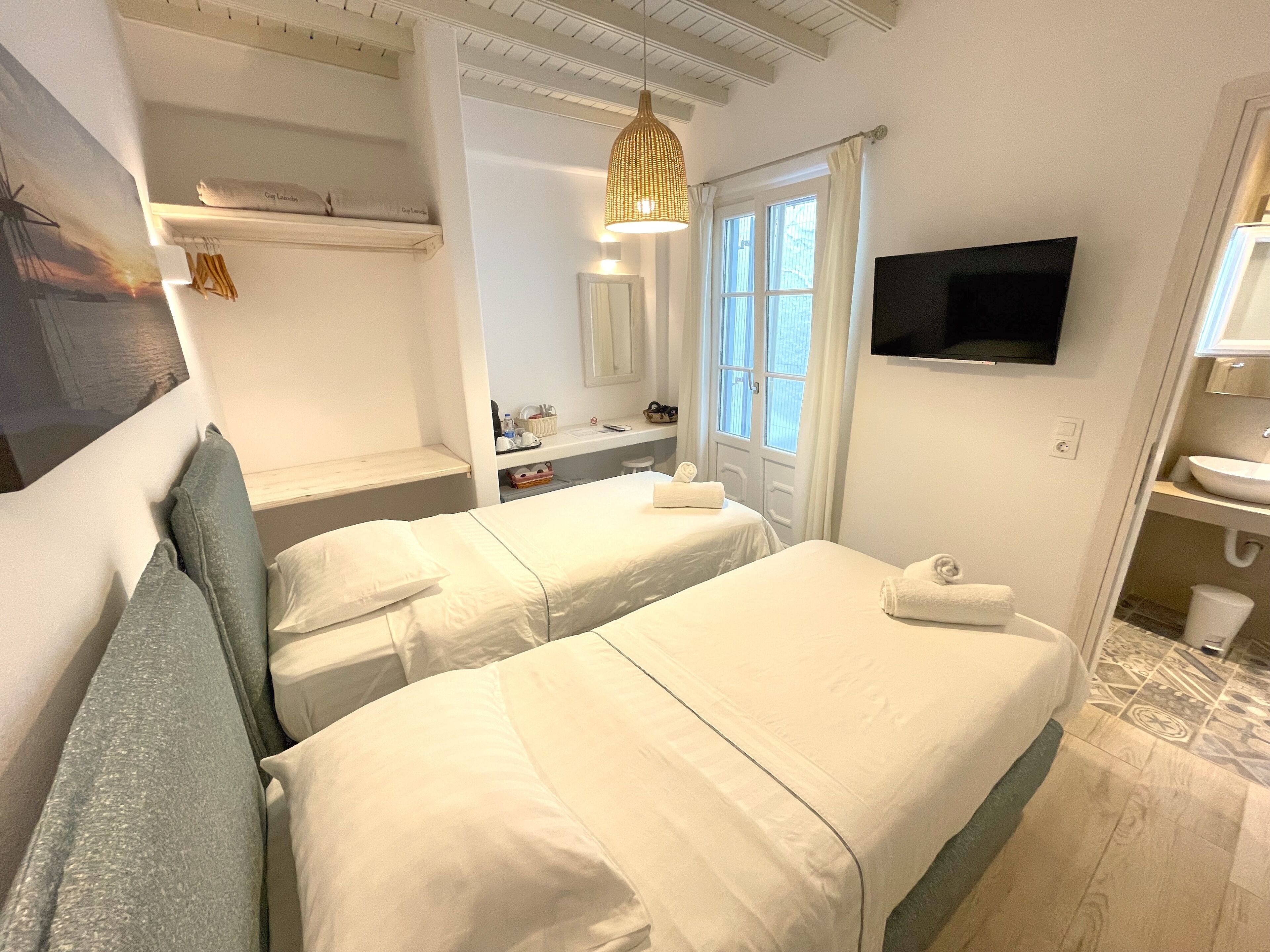 Quarto de hotel com duas camas, televisão fixada na parede, banheiro com pia e espelho, e janela com cortinas.