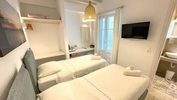 Quarto de hotel com duas camas, televisão fixada na parede, banheiro com pia e espelho, e janela com cortinas.