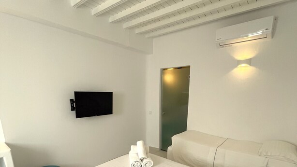 A hotel room with a large bed, a flat-screen TV mounted on the wall, and a ceiling light fixture. - Hotel Lefteris (Mykonos)