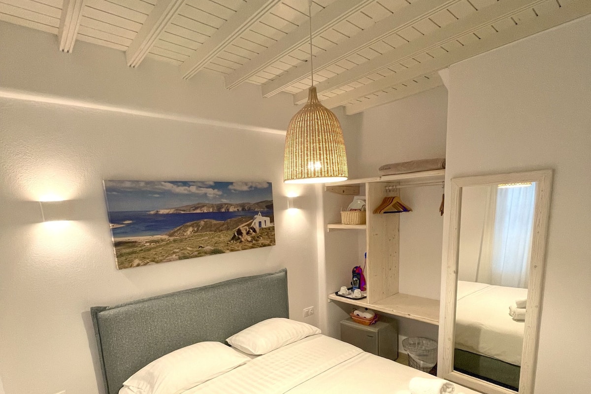 Um quarto com cama, luminária pendente, espelho e prateleira na parede.