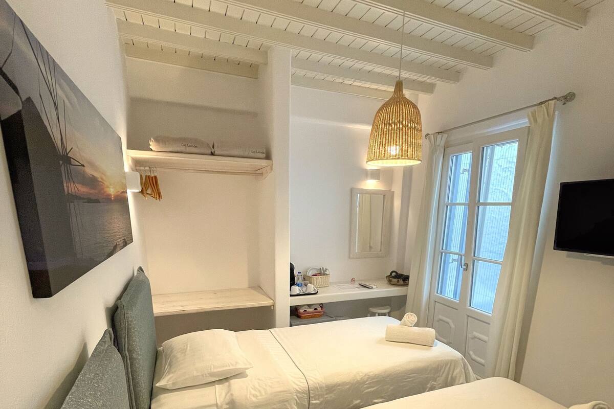 Quarto de hotel com duas camas, banheiro com espelho e televisão na parede.