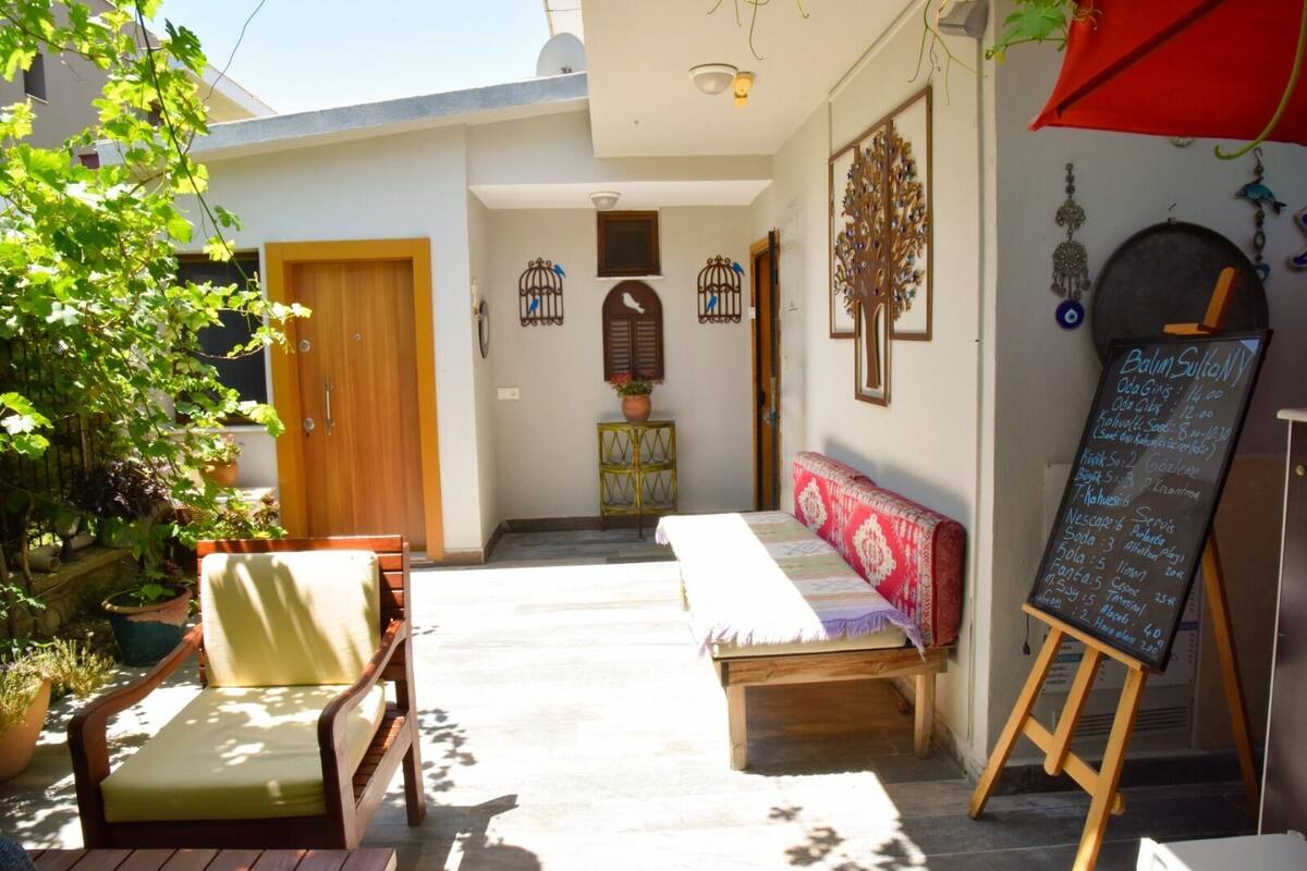A cozy outdoor seating area with a bench and chairs, a wooden door, and a chalkboard menu.