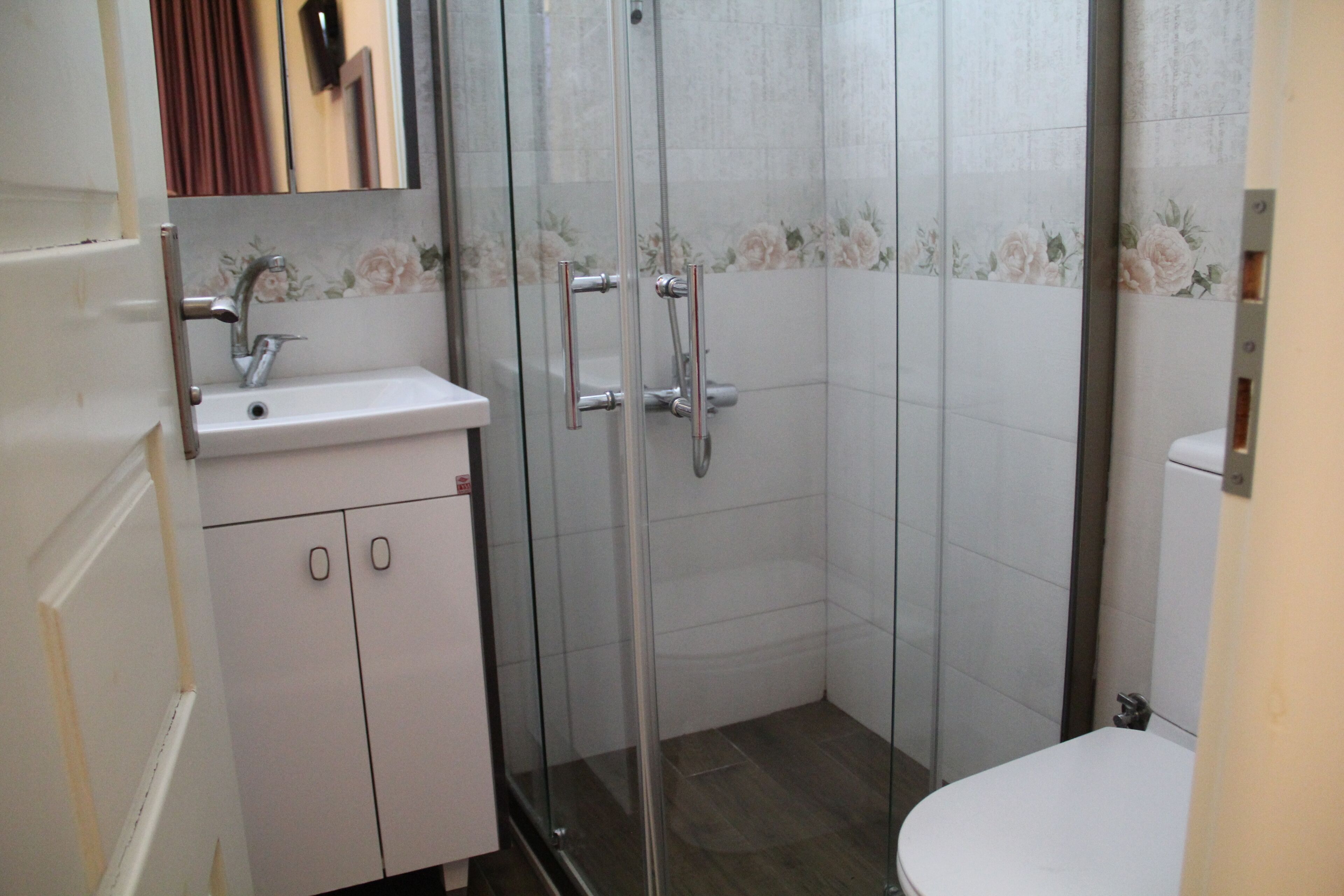 A bathroom with a glass-enclosed shower, a sink with a mirror, and a toilet.