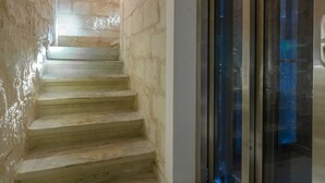 Un escalier avec des murs en pierre et une porte d’ascenseur en verre.