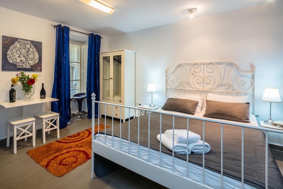 A bedroom with a bed, bedside tables, a desk, a chair, a wardrobe, and a window with curtains.