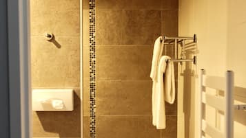 Un baño con ducha, un perchero para toallas y un dispensador de papel higiénico.