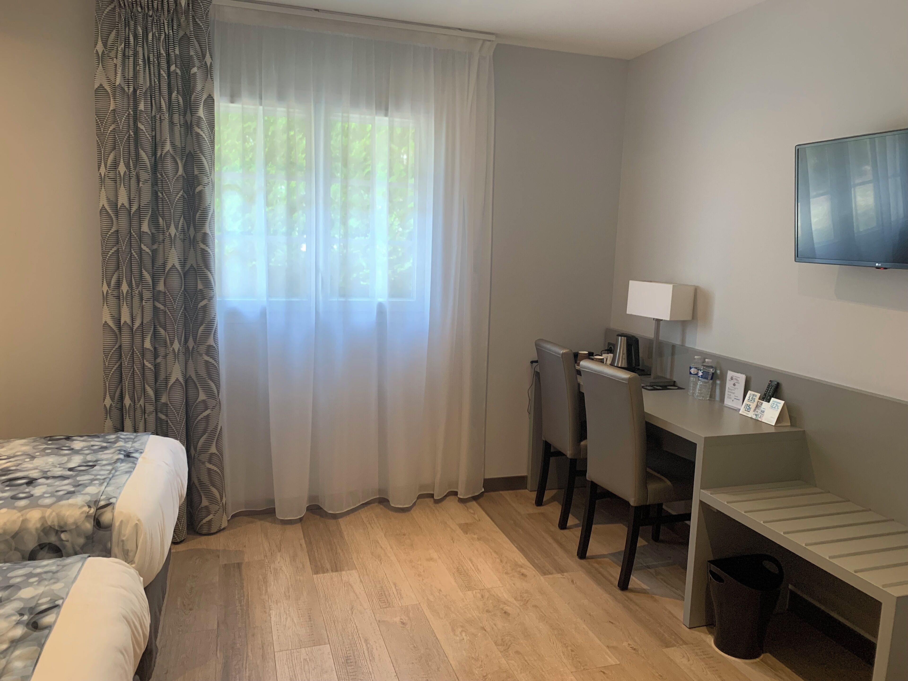 Camera d'albergo con un letto, una scrivania, una sedia, una televisione e una finestra con tende.