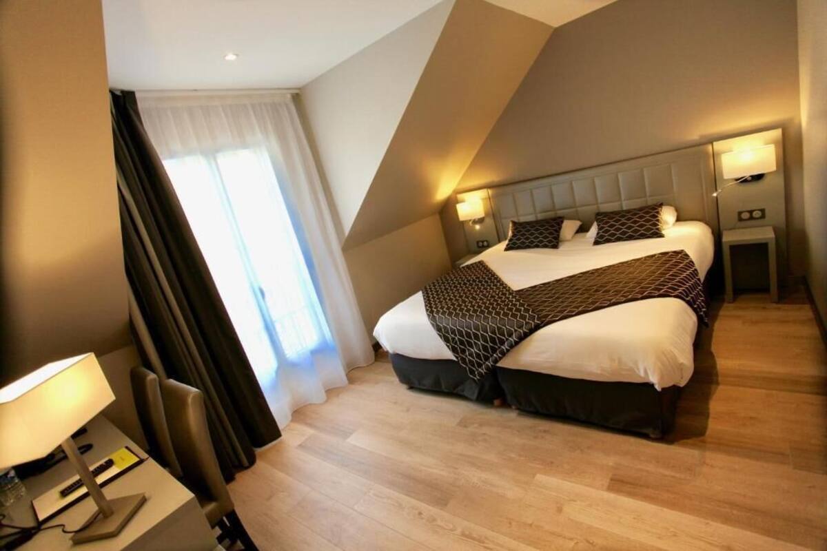 Una habitación de hotel con una cama grande, mesitas de noche, un escritorio y una ventana con cortinas.