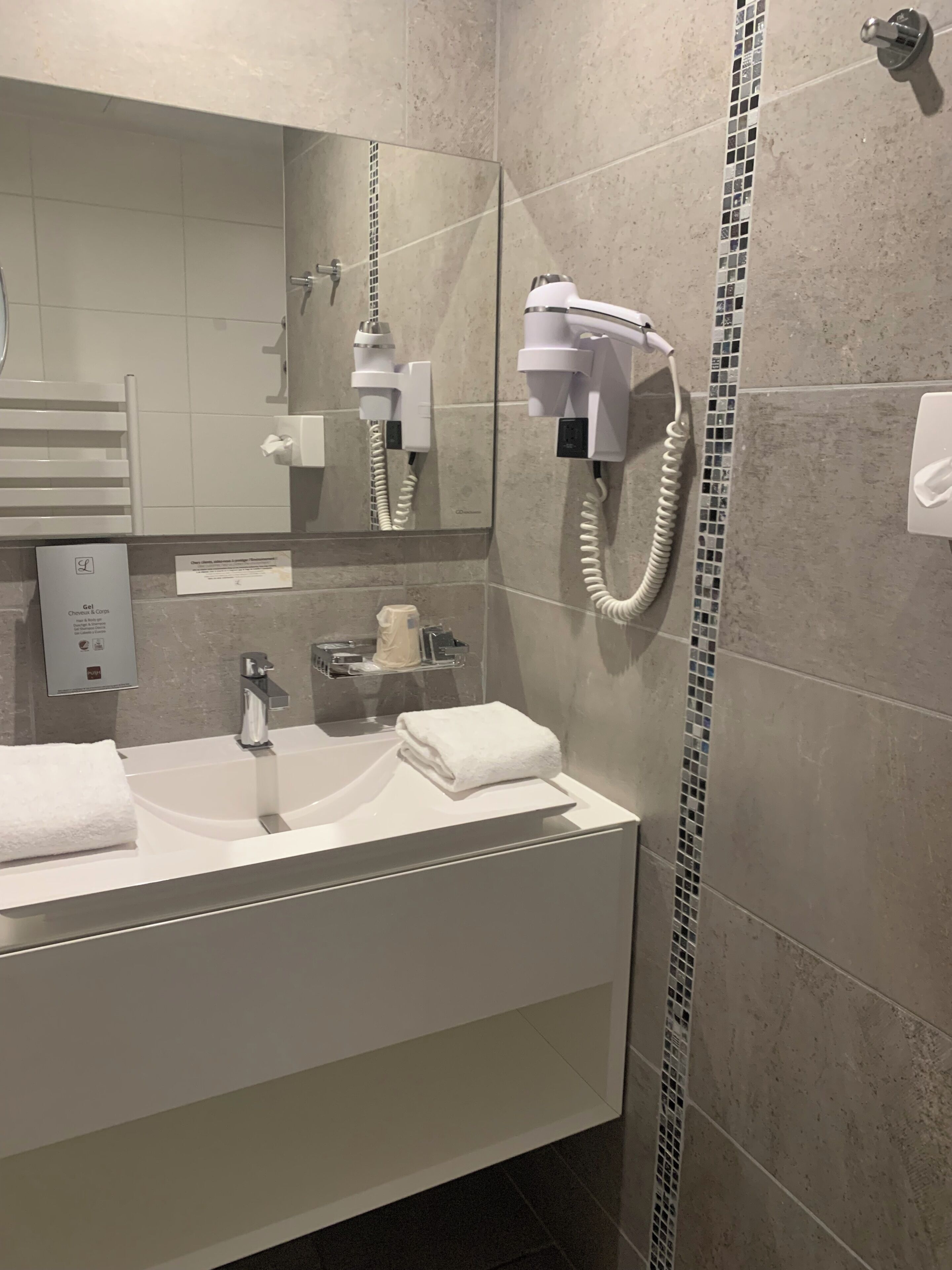 A modern bathroom with a large mirror, a sink, a hairdryer, and a towel rack.