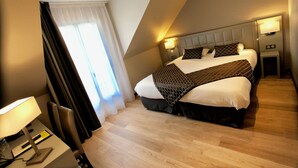 Una habitación de hotel moderna con una cama grande, una mesita de noche con lámpara, y un ventanal con cortinas.