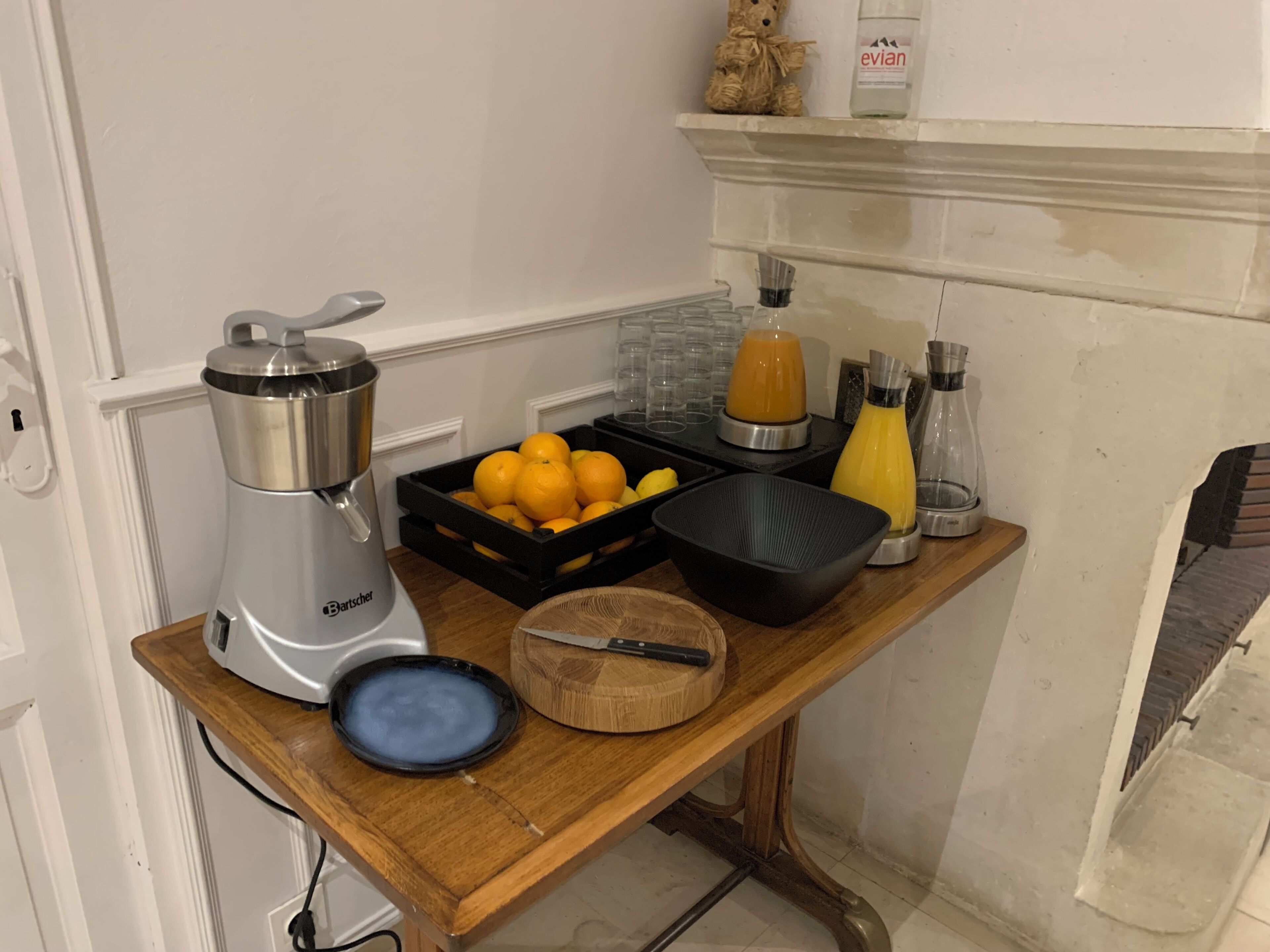 Een keukenblad met een koffiezetapparaat, een fruitmand, een snijplank, een mes en een fles sap.
