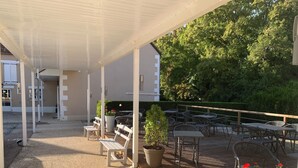 Un patio al aire libre con mesas y sillas, una zona de estar cubierta y plantas en macetas.