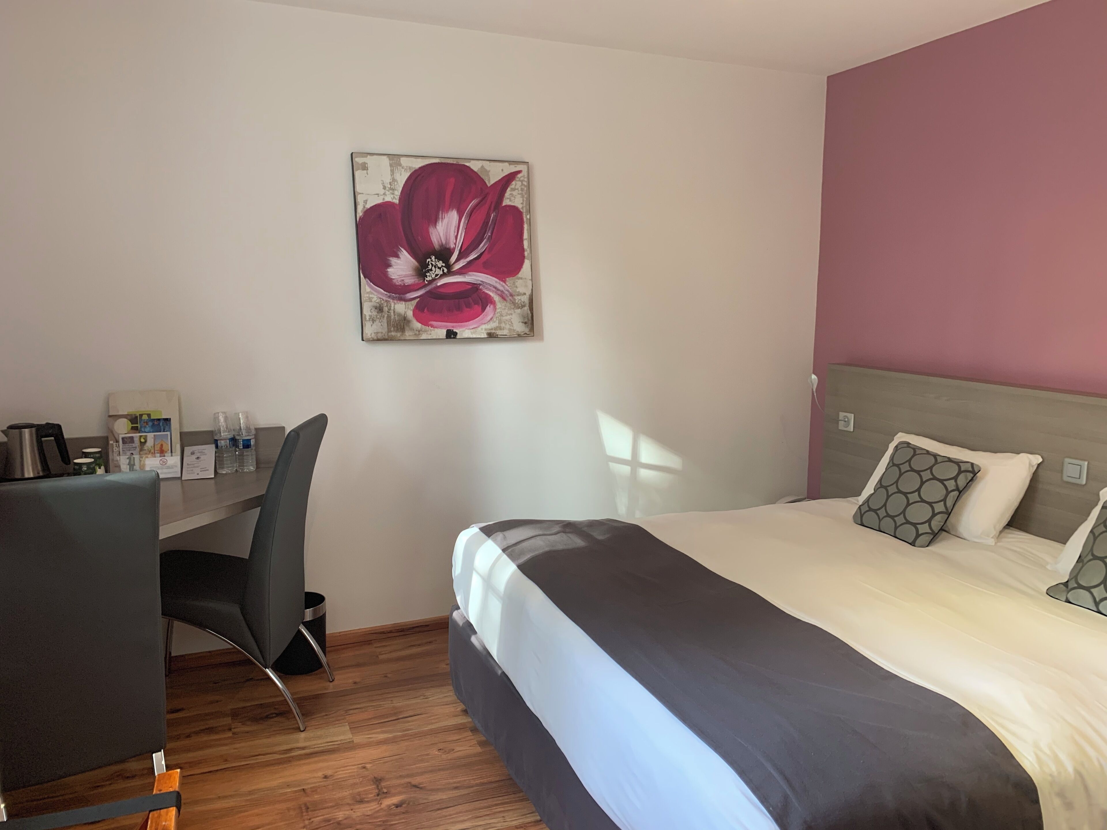 Een hotelkamer met een bed, een bureau, een stoel, een schilderij en een houten vloer.