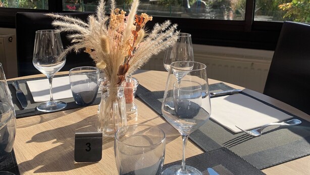Una mesa dispuesta con copas de vino, un florero con plantas secas y un número.