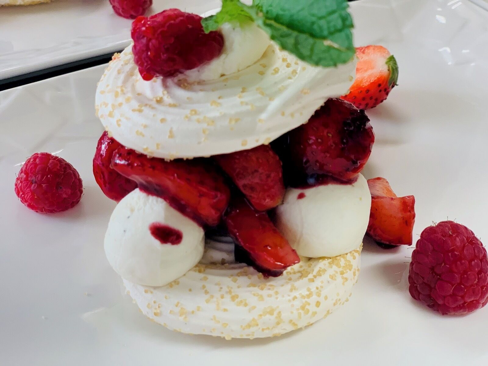 Postre amb merengue, fresons, frambueses i una fulla de menta.
