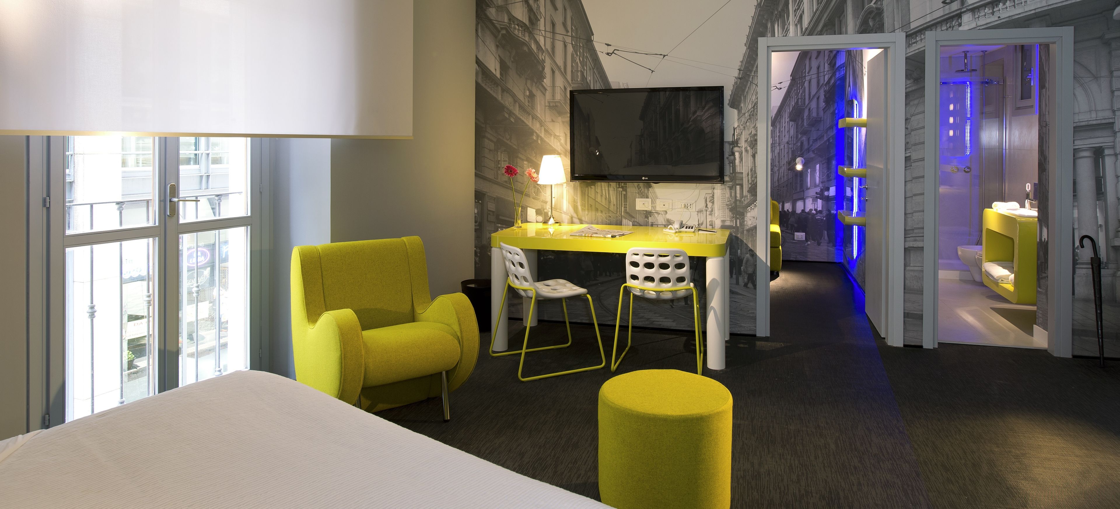Et moderne hotelværelse med en stor seng, et skrivebord med stol, et fjernsyn og et badeværelse med bruser.